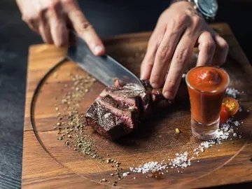 Fleisch wird auf einem Holzbrett geschnitten, mit Sauce daneben.